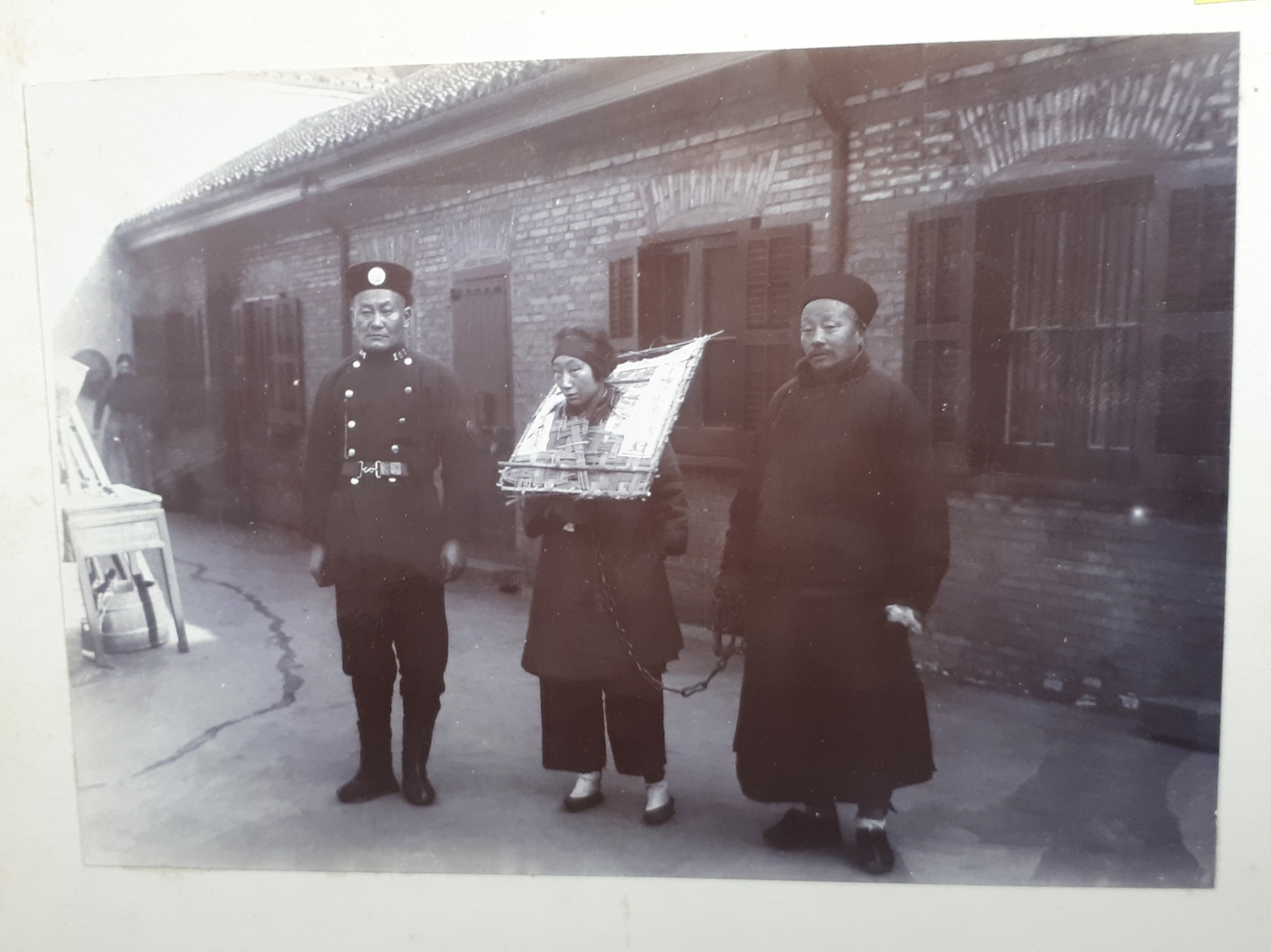 Police with a prisoner receiving the ‘cangue’ treatment, a device used for public humiliation and corporal punishment.