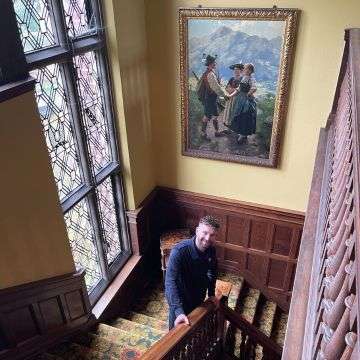 Tom Winterton on the stairs at The Grange. On the wall is Emil Rau’s alpine scene ‘The Encounter’.